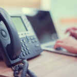 Close Up On Telephone With Employee Man Working On Laptop At Off